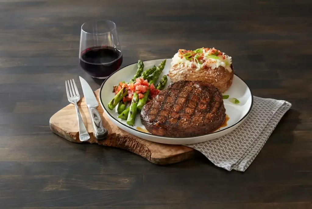 Plated grilled steak, baked potato, and asparagus with red wine.