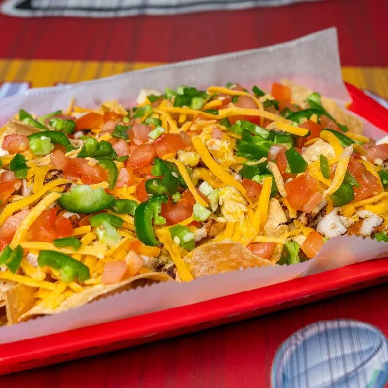 Close-up of nachos with cheese, tomatoes, jalapeños in a red tray.