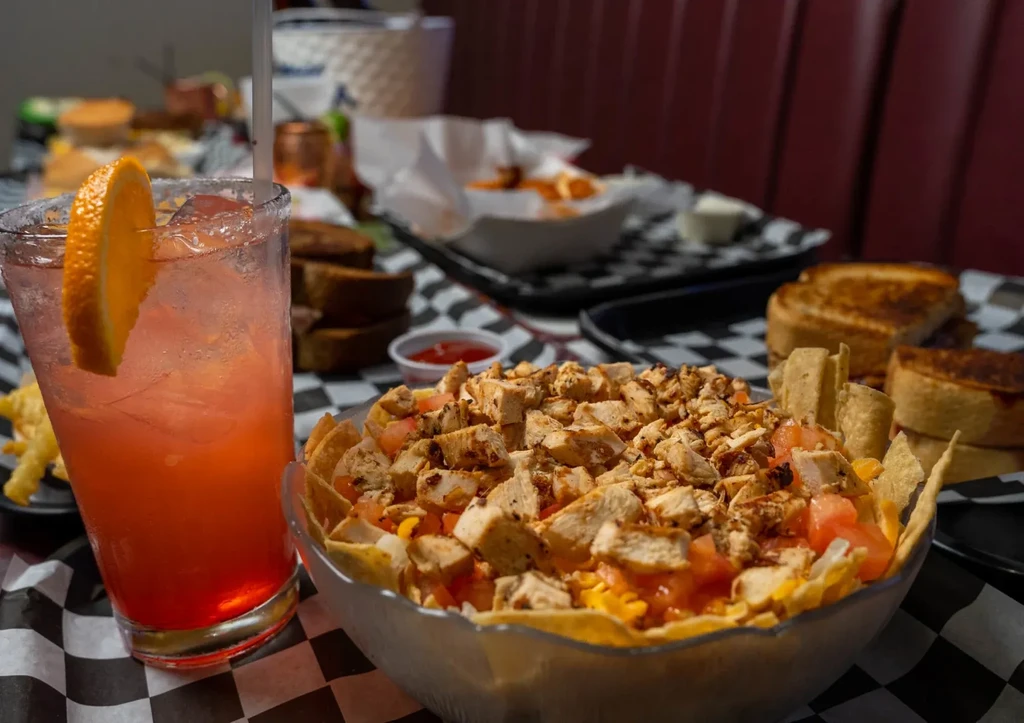 Chicken nachos and an iced orange drink on a checkered diner table.