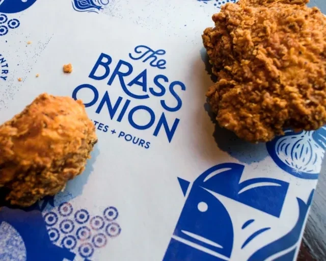 Two crispy fried chicken pieces on "The Brass Onion" branded white surface.