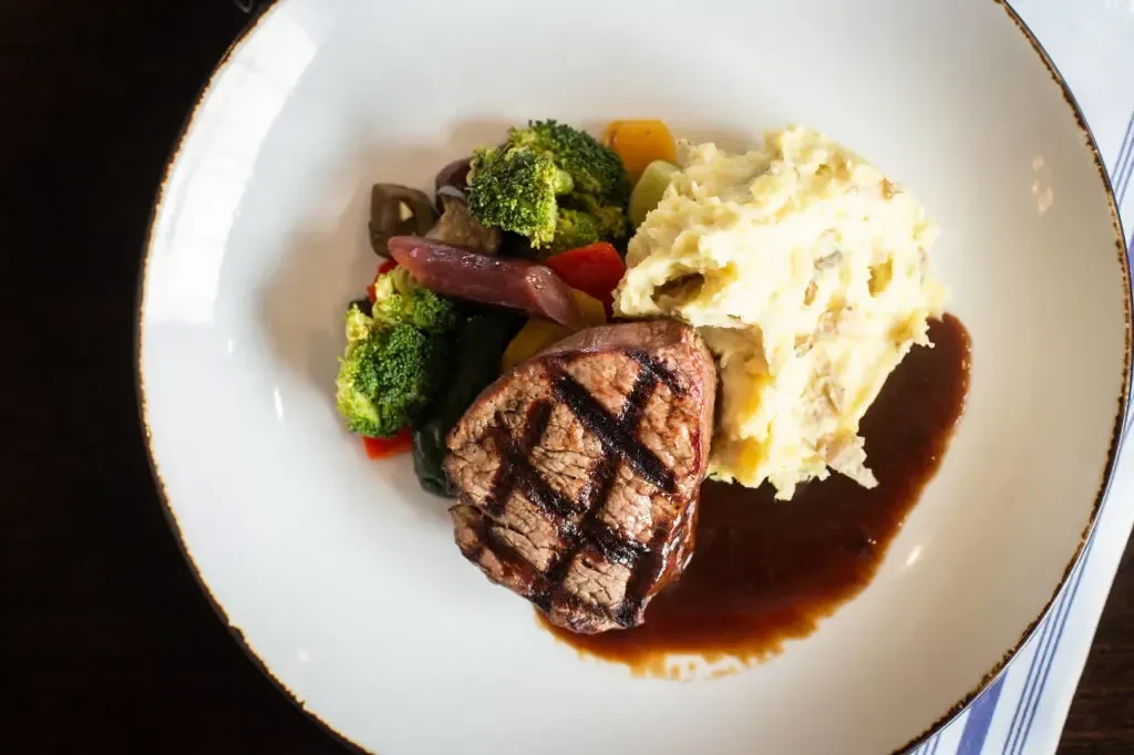 Plated grilled steak with mashed potatoes and colorful vegetables.