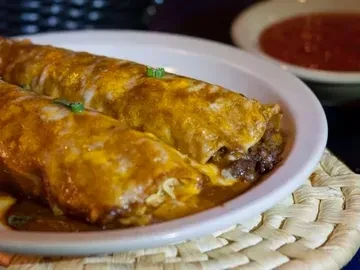 Two meat enchiladas with melted cheese, reddish sauce, and green herbs.