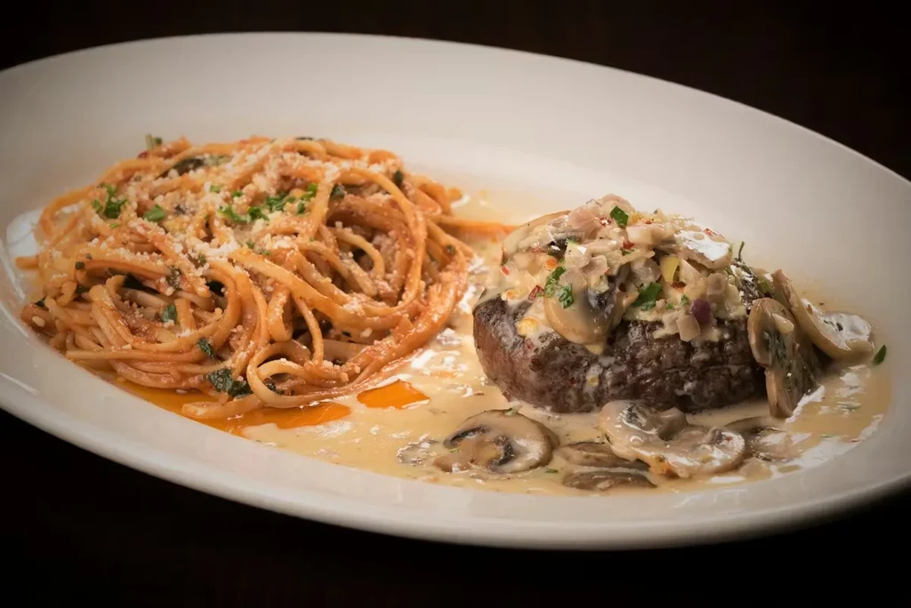 Plated beef steak with creamy mushroom sauce and cheesy linguine.