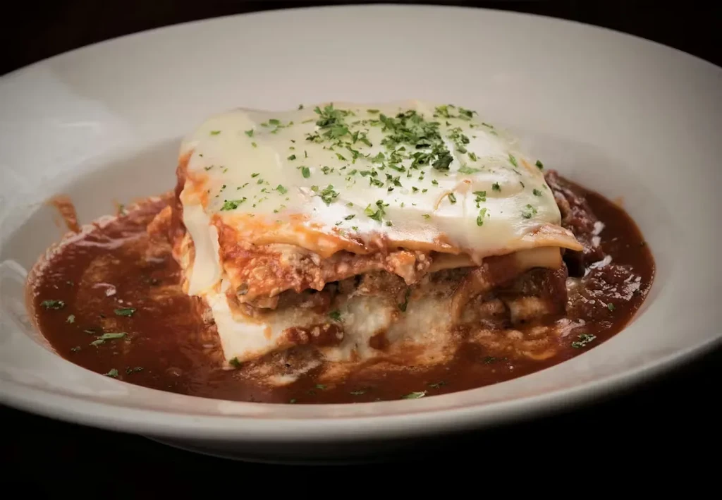 Layered lasagna with melted cheese, green herbs, in red sauce.