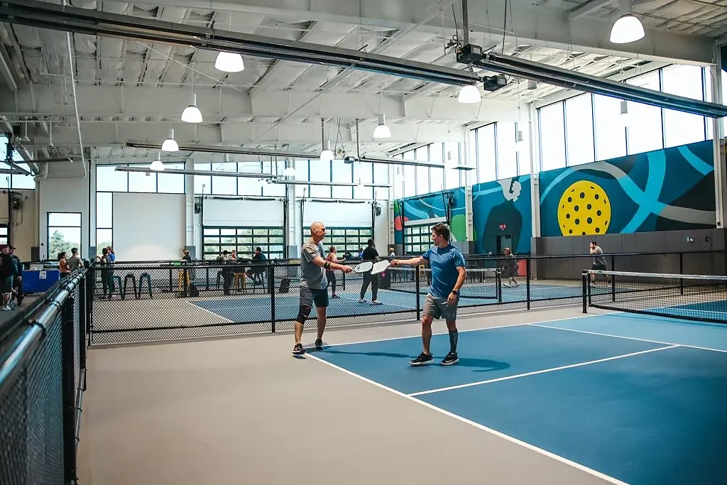Two players on indoor blue pickleball courts with mural