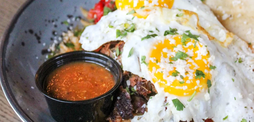 Sunny-side-up eggs, shredded meat, cheese, herbs, salsa, and tortilla on a plate.