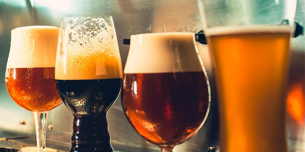 Four distinct beers in various glasses with foam on a bar.