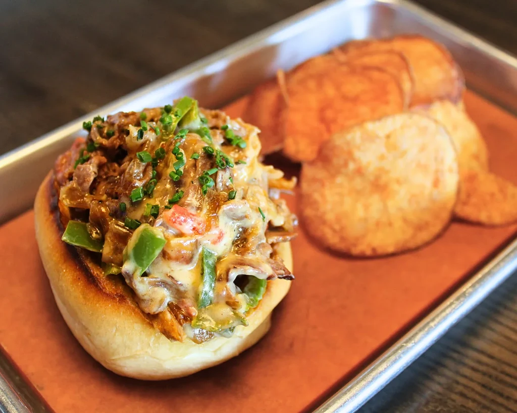 Golden bun with meat, melted cheese, green peppers, chives, and chips.