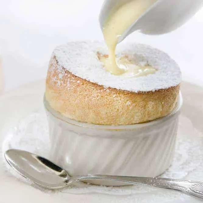 Soufflé in ramekin with powdered sugar, crème anglaise being poured.