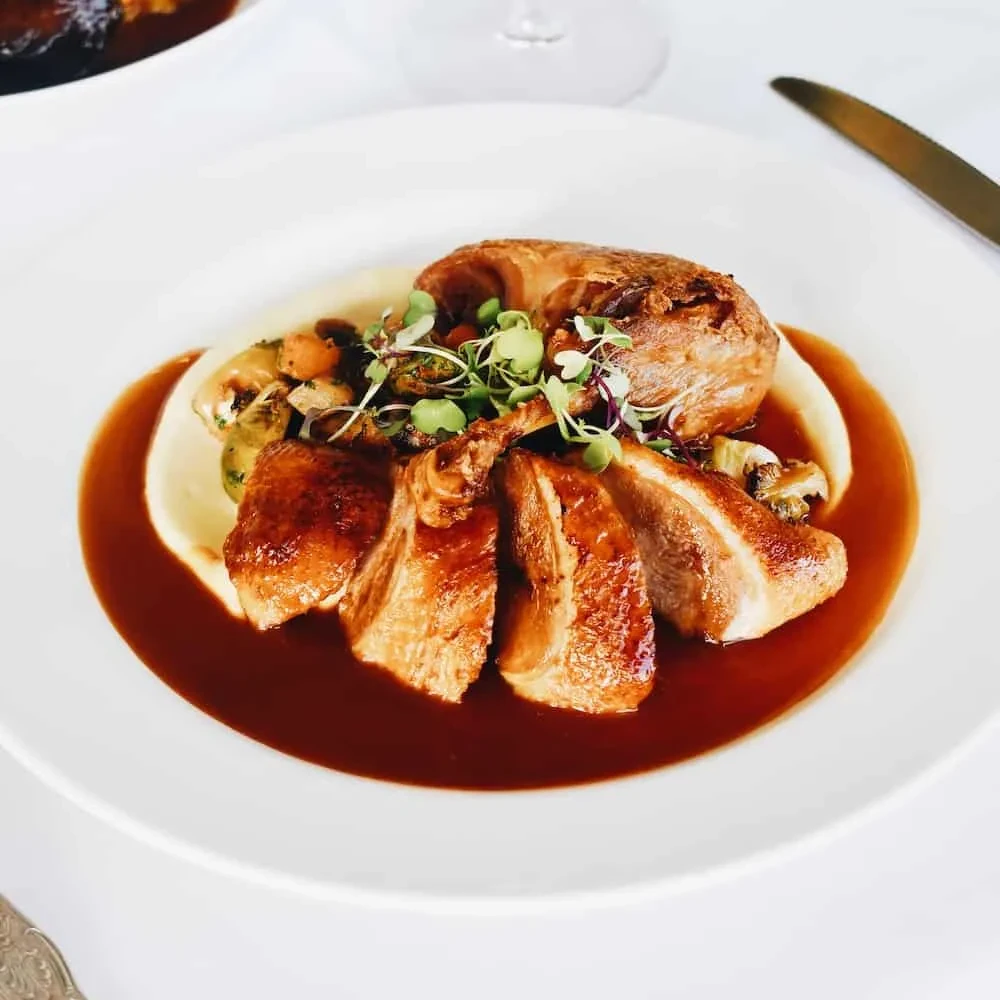 Plated crispy poultry, creamy purée, vegetables, and dark sauce.