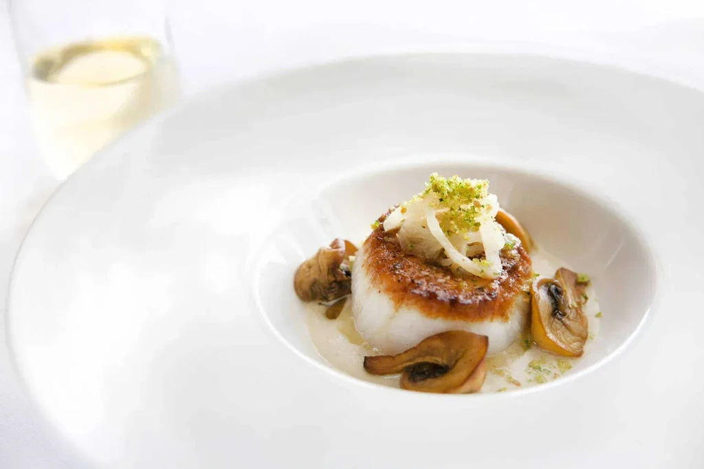Finely plated seared fish/scallop, mushrooms, green garnish, and creamy sauce.