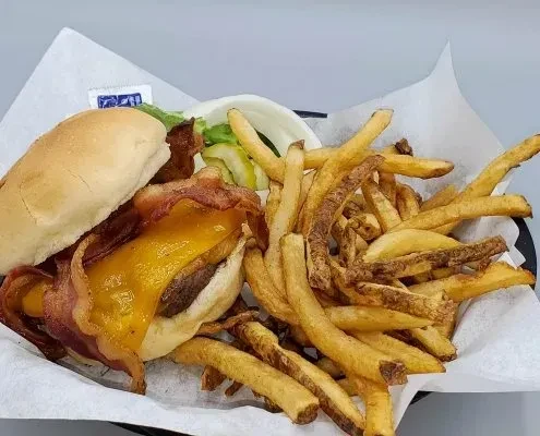 Classic bacon cheeseburger and fries served in a black basket.
