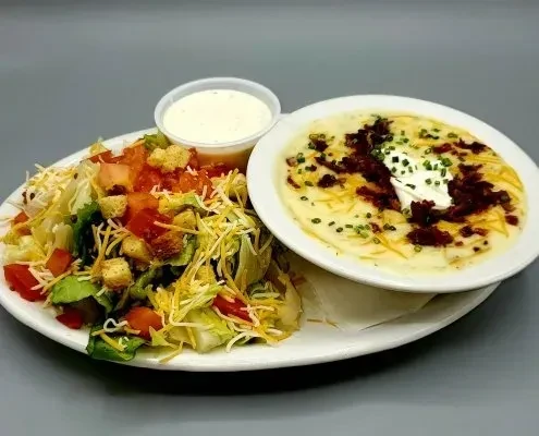 A side salad and creamy soup topped with cheese, bacon, and chives.