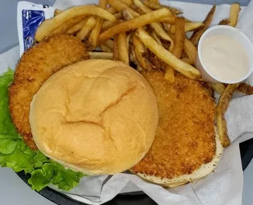 A large fried chicken sandwich, fries, and dipping sauce in a basket.