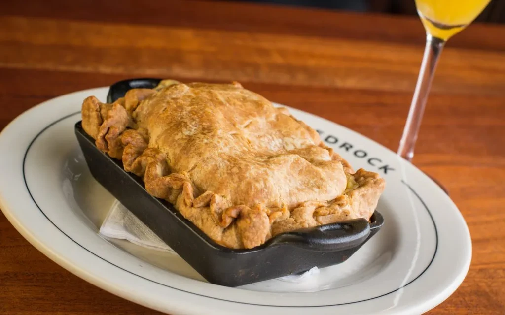 Savory pie with flaky crust in cast iron dish on "BEDROCK" plate.