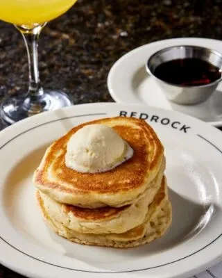 Pancakes with melting butter, syrup, and orange juice on a "REDROCK" plate.