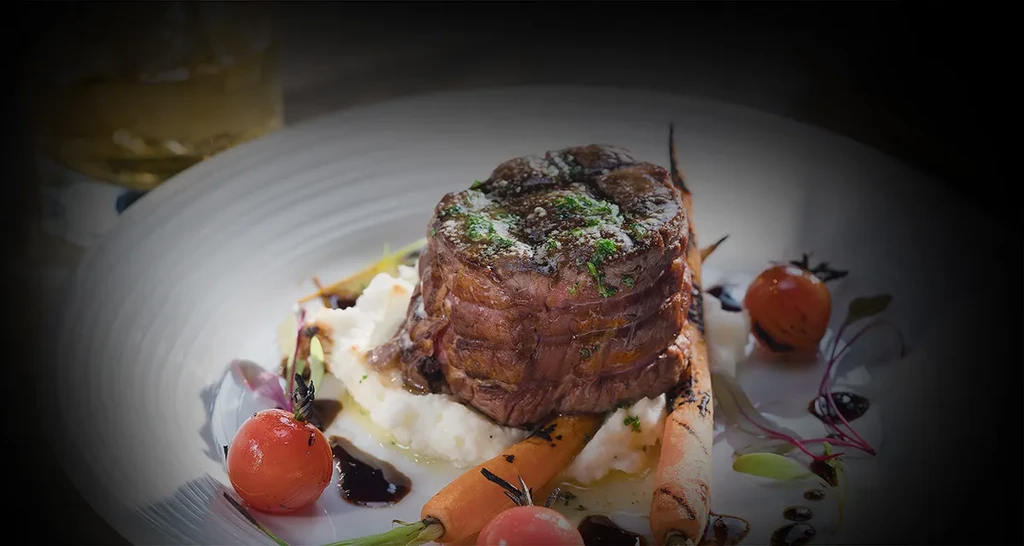 Seared steak, mashed potatoes, roasted carrots, tomatoes, and microgreens.