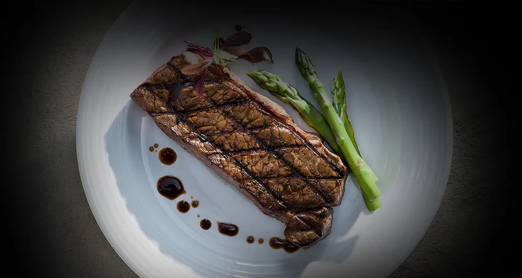 Grilled steak with grill marks, asparagus, dark sauce, and microgreens.