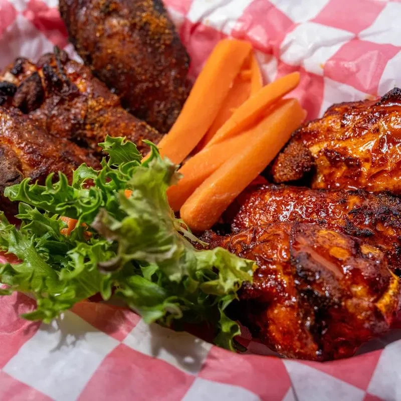 Close-up of chicken wings, baby carrots, and lettuce in a checkered container.