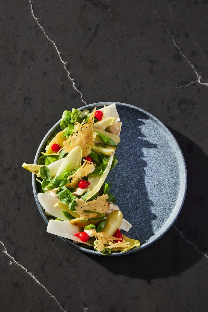 Crescent-shaped salad with greens, red berries, and crispy elements.
