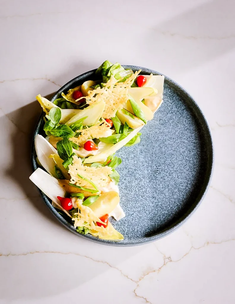 Artfully plated salad with endive, red elements, and crispy cheese.
