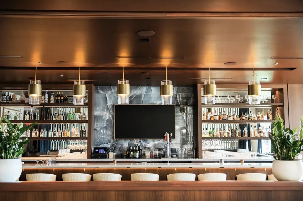 Empty, upscale modern bar with curved wooden counter, stocked shelves.