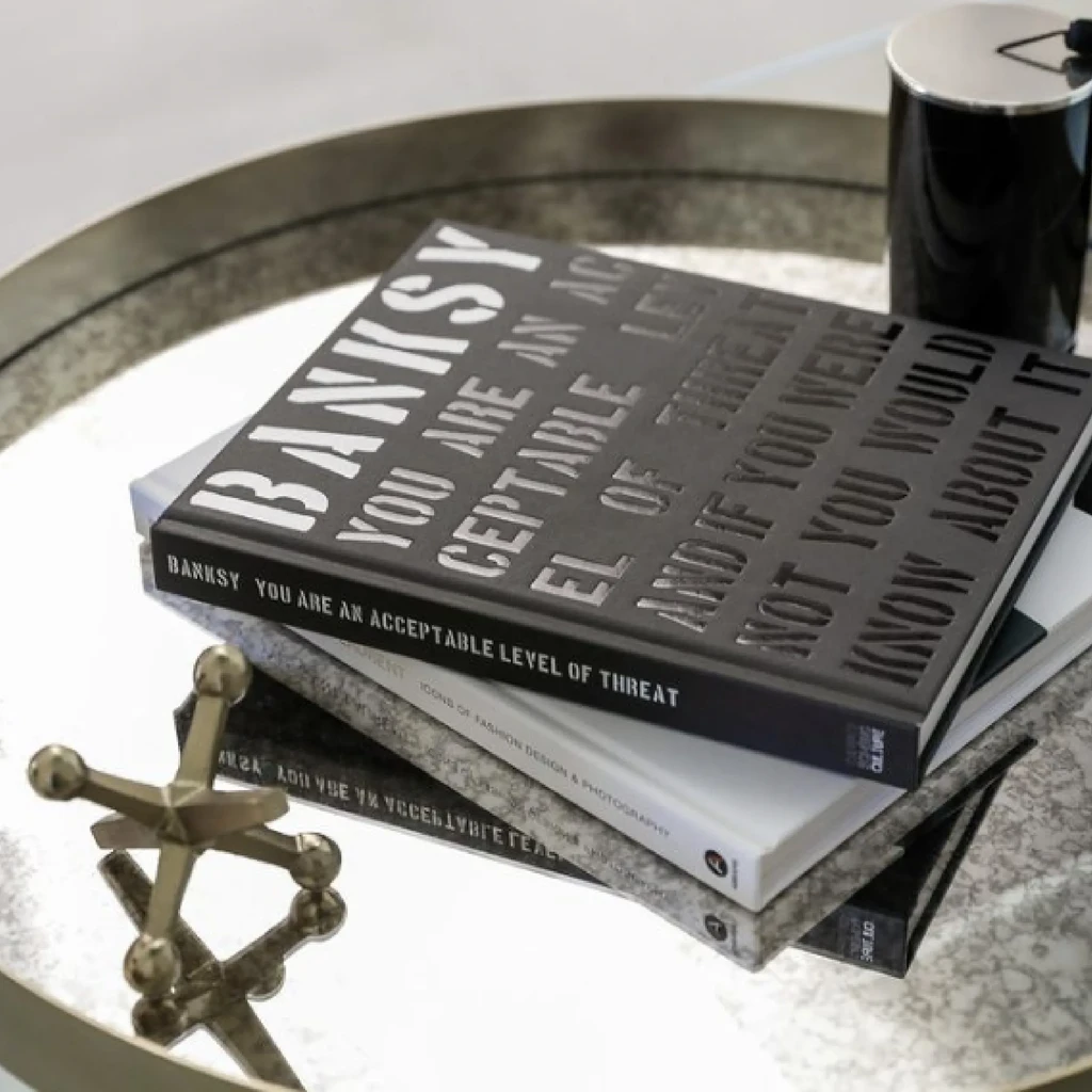 Banksy book tops a stack, alongside a starburst on a metallic tray.