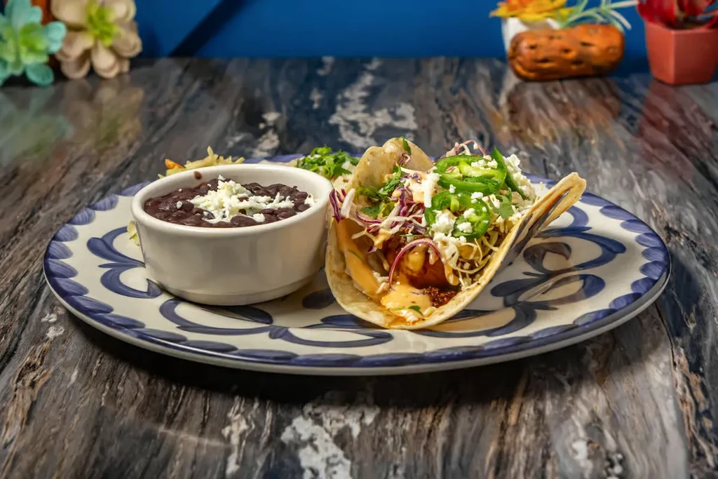 Close-up of a fried protein taco with jalapeños, beans, and cheese.
