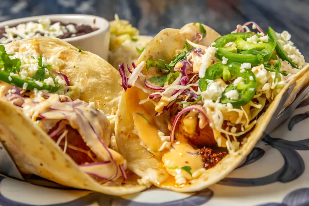 Two soft-shell tacos with cabbage, cheese, jalapeños, and sauce.