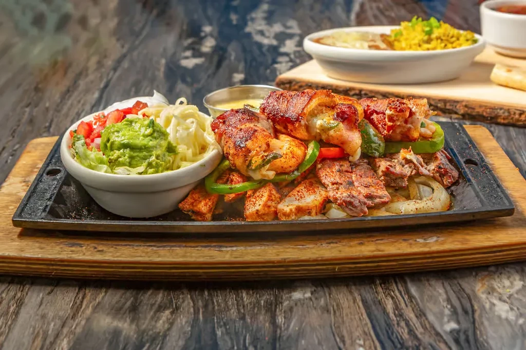 Sizzling cast iron platter with chicken, steak fajitas, and sides.