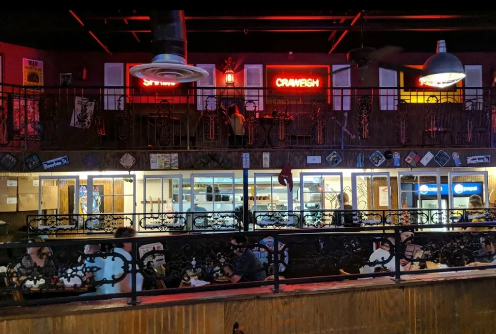 Multi-level restaurant interior with diners, neon signs, and a Bourbon St. sign.
