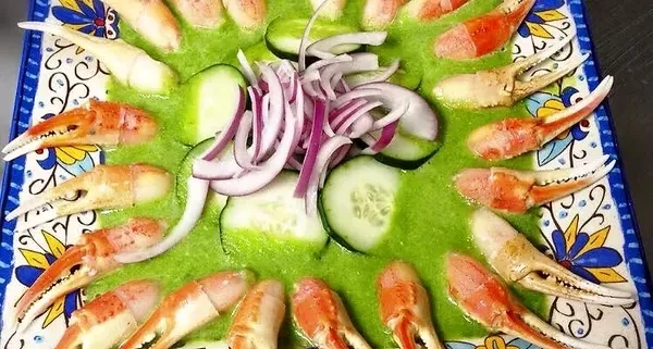 Seafood appetizer with crab claws, green sauce, cucumbers, and red onions.