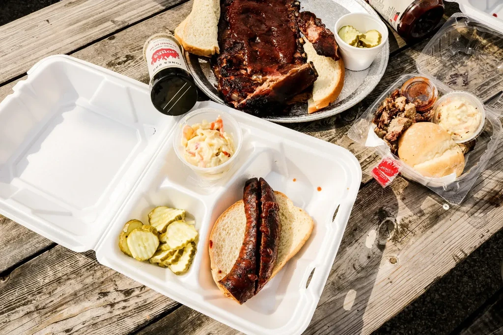 Top-down view of barbecue ribs, sausage, and sides on a wooden table.