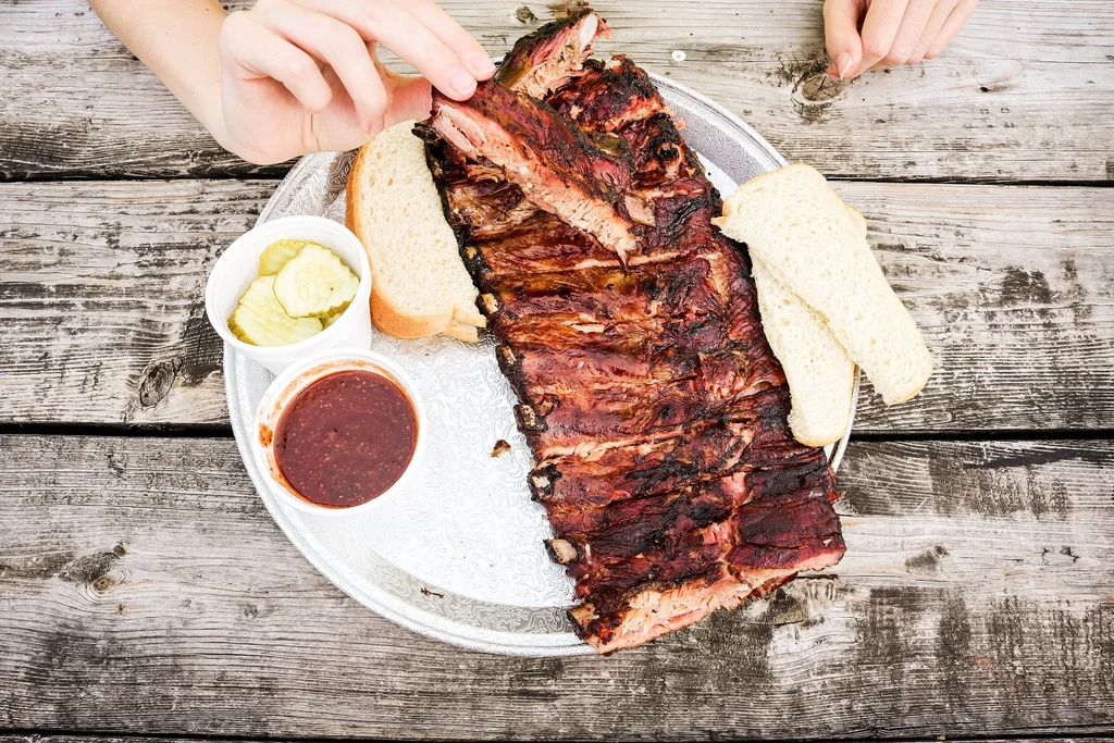 Hands pull saucy barbecue ribs, served with bread and pickles.