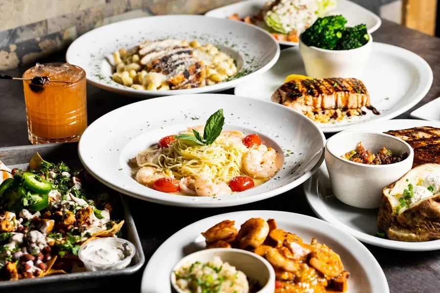Overhead shot of a dark table with multiple dishes and a cocktail.