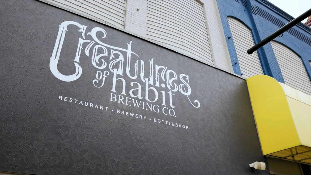White, decorative Creatures of Habit Brewing Co. sign on gray wall.