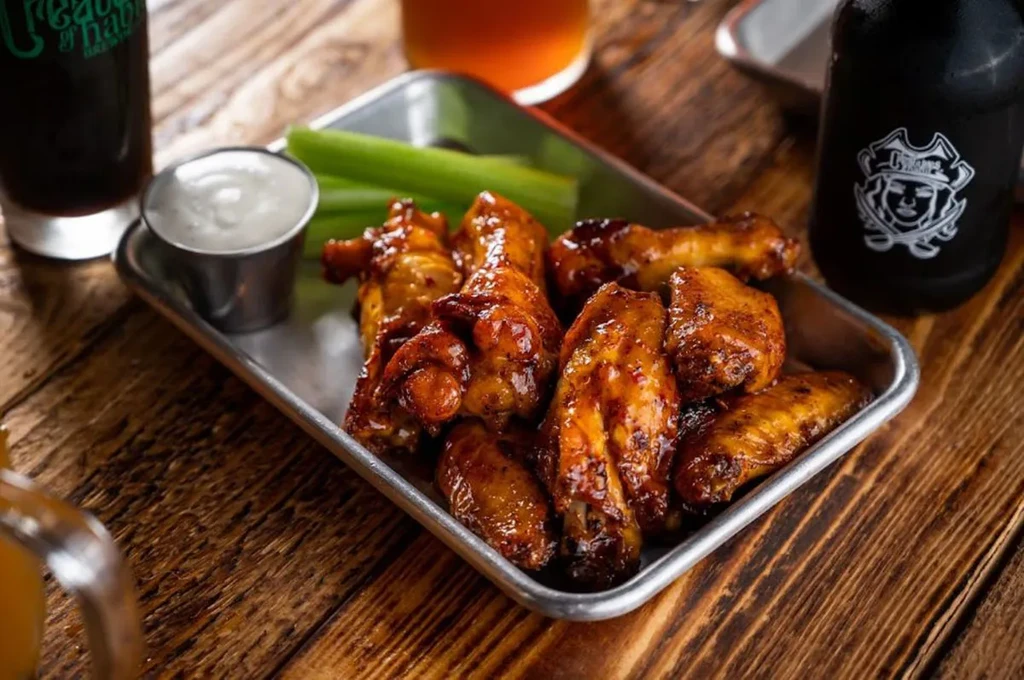 Golden-brown chicken wings, white dipping sauce, and celery on a wooden table.