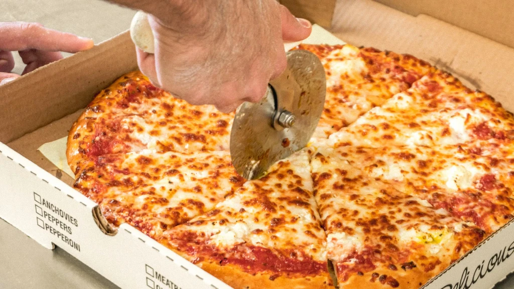 Person's hands cutting a freshly baked cheese pizza inside its box.
