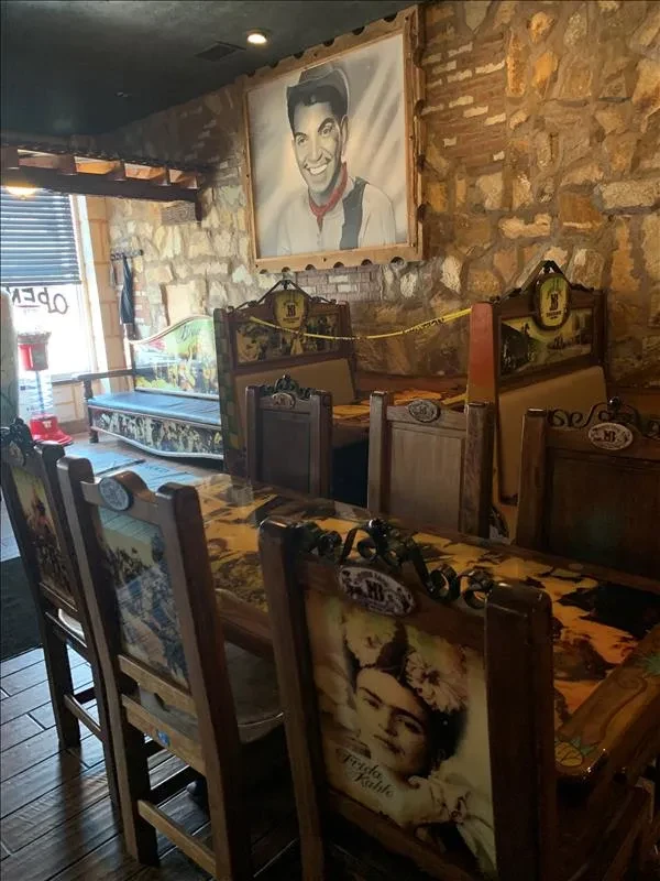 Rustic restaurant interior with stone walls, portrait, and Frida Kahlo chair.