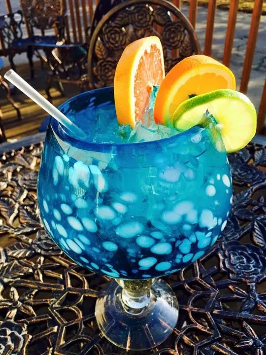 Blue cocktail with citrus slices and ice in a spotted glass outdoors.