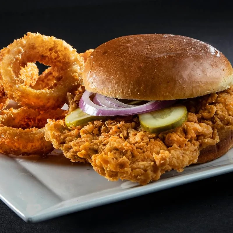 Golden fried chicken sandwich with pickles, red onion, and crispy onion rings.