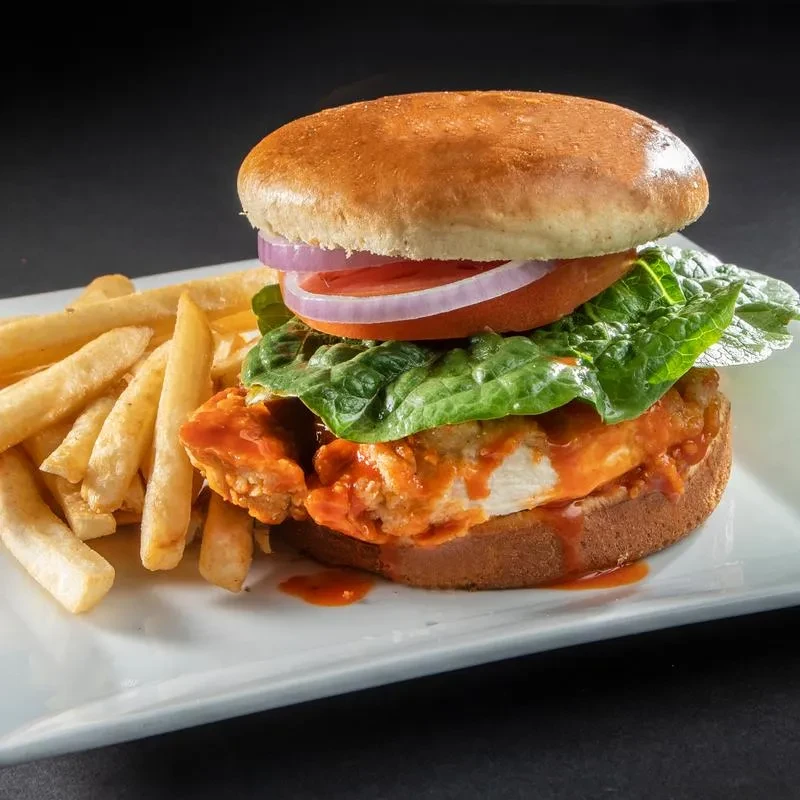 Fried chicken sandwich with buffalo sauce, lettuce, tomato, onion, and fries.