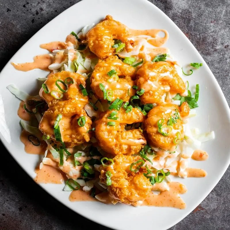 Golden-brown fried shrimp with creamy and orange sauces, green onions.