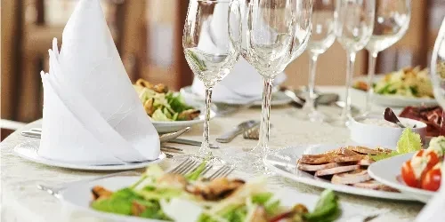 Elegant dining table with multiple place settings of salads and meat.