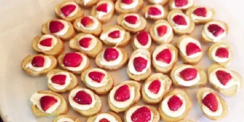 Small desserts topped with cream and halved red strawberries.