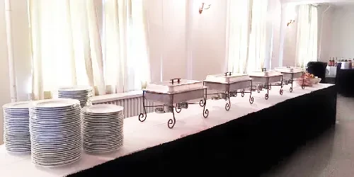 Buffet setup with plates, chafing dishes, and fruit in an event hall.