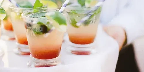 Mojito-style cocktails with mint, lime, and straws on a white tray.