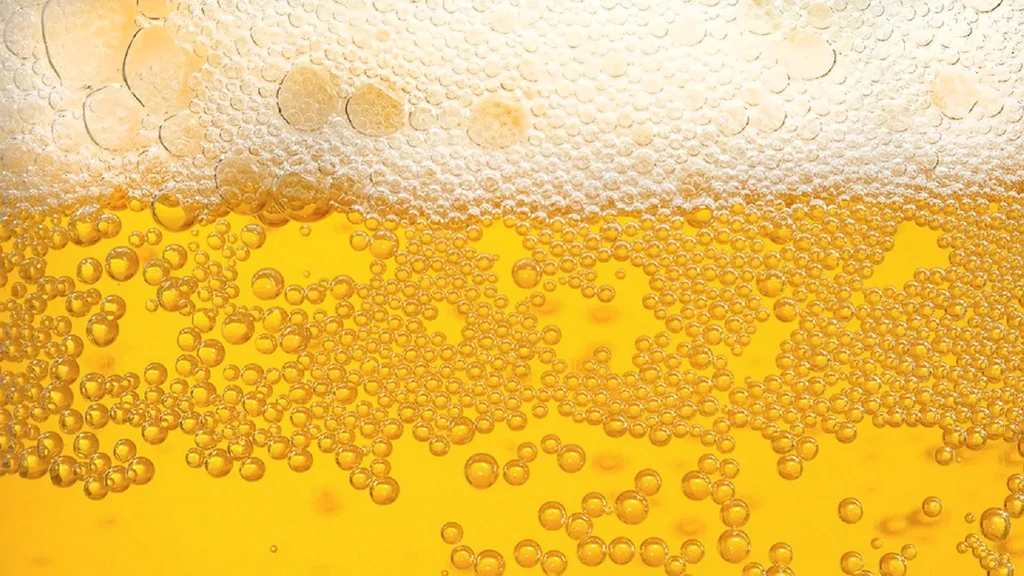 Close-up of golden carbonated beverage, rising bubbles, and thick white head.