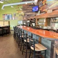 Empty bar with reddish-orange counter, rustic wood wall, and green wall.