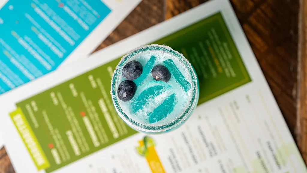 Top-down, bright blue cocktail with blueberries and blue ice.